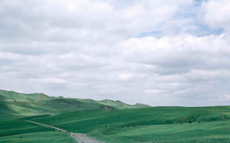 countryside road between green mountains under cloudy sky